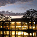 View of the front of Thomas Cooper Library in early evening, taken from across the reflecting pool. The lights from the library windows are reflected on the water.